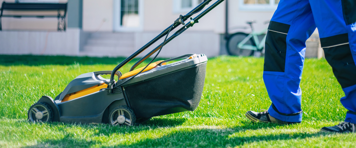 Person in blue and black pants mowing the grass with a green and yellow lawn mower